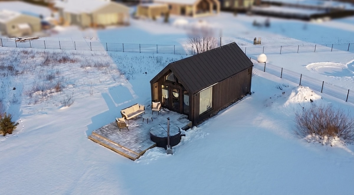 Aerial view of the Pirts Rīga cabin with outdoor patio, seating and hot tub in a snowy winter landscape